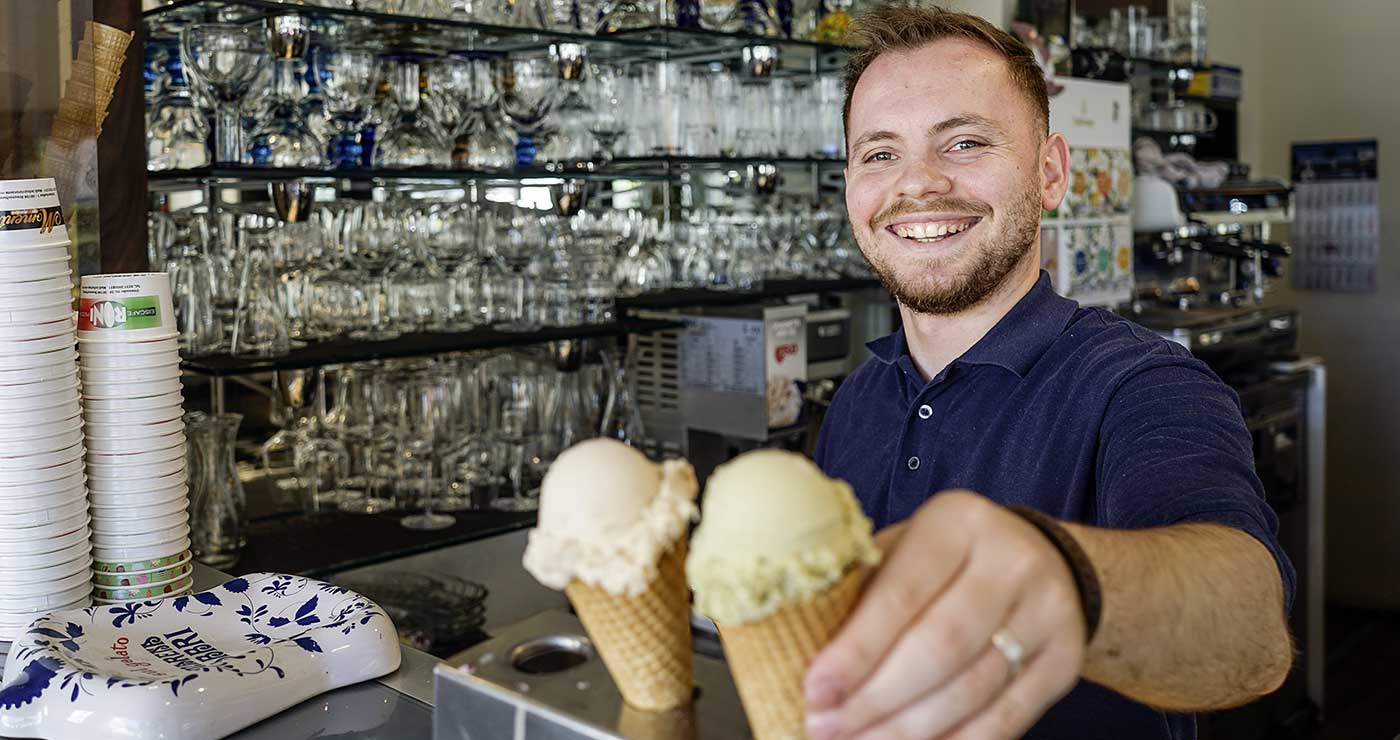 Strahlender Mitarbeiter des Roni mit zwei Eiswaffeln an der Eistheke