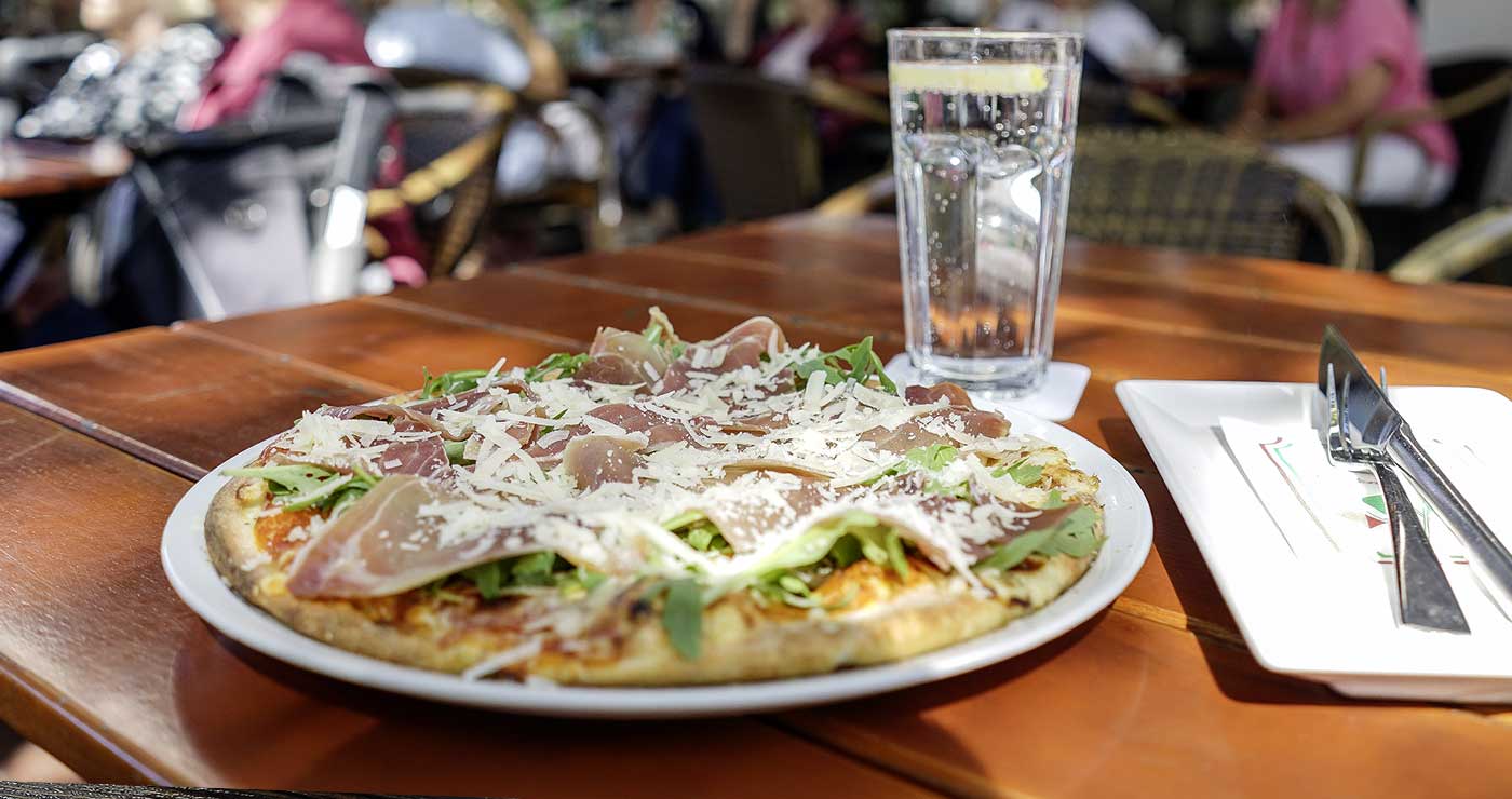 Pizza mit Rucola und Parmesan auf der Terrasse des Roni
